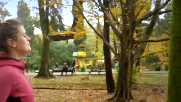 Mulher bonita com cabelos longos correndo no parque de outono. vista lateral — Vídeo de Stock