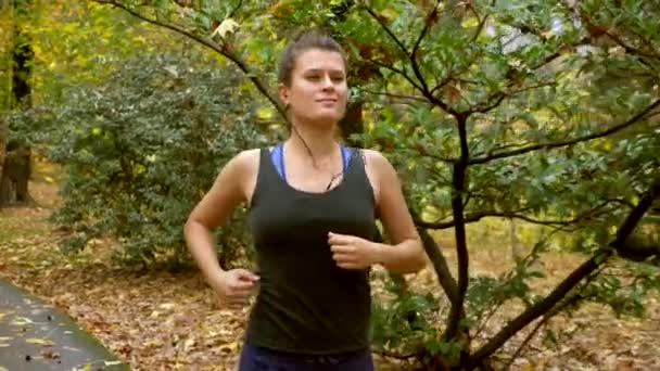 Chica deportiva con auriculares trotar en otoño Parque — Vídeos de Stock