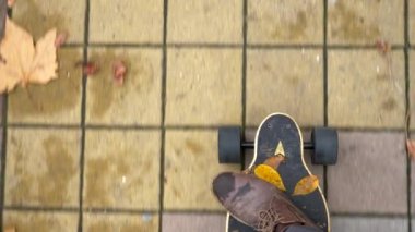 Yukarıdan bak. Erkek bacaklarının elektrikli bir kaykayın üzerinde, sonbahar yapraklarıyla kaldırımda sürerken yakın çekimi.