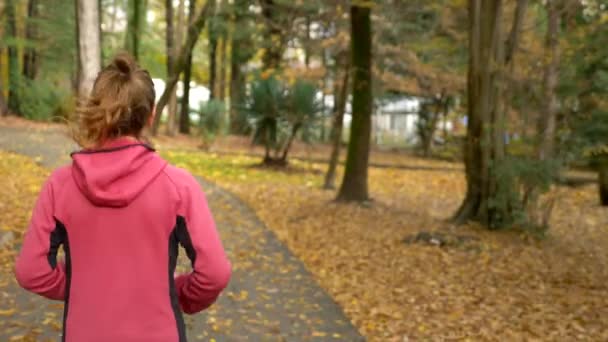 Atletisch jong meisje rennen in de herfst Park na regen. achteraanzicht — Stockvideo