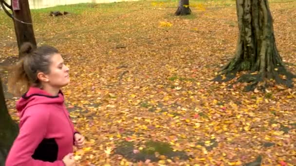 Gyönyörű nő hosszú hajjal kocog az őszi parkban. oldalnézet — Stock videók