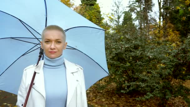 Stílusos szőke nő rövid haj séták a parkban esernyő — Stock videók
