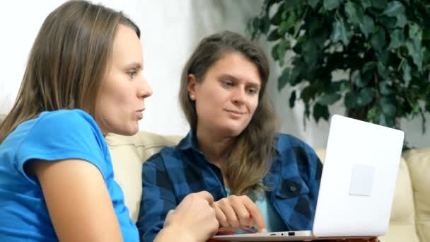 Две девочки сидят вместе на диване в гостиной и используют ноутбук — стоковое видео