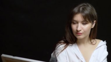 Güzel kız ressam tuvale yağlı boyalarla resim yapıyor. siyah arkaplan