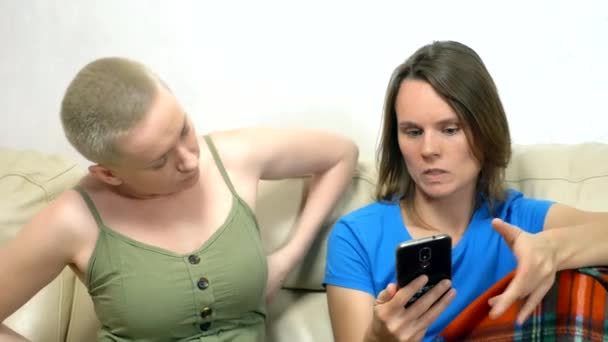 Dua wanita menggunakan smartphone saat duduk bersama di sofa — Stok Video