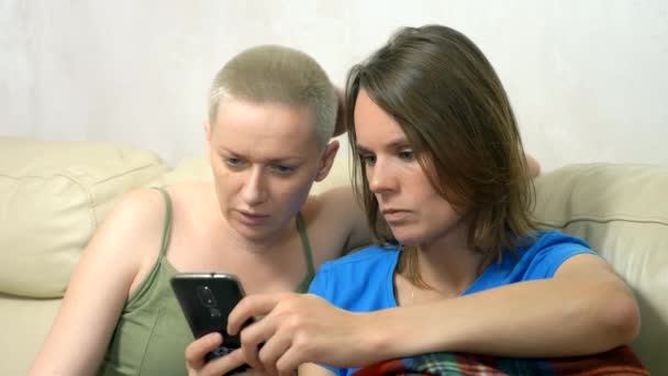 Two women using a smartphone while sitting together on the sofa — Stock Video