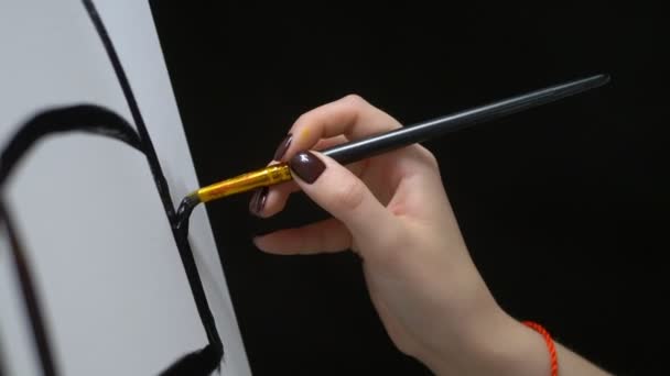 Closeup. female hand painting with a brush a black line on a clean white canvas — ストック動画