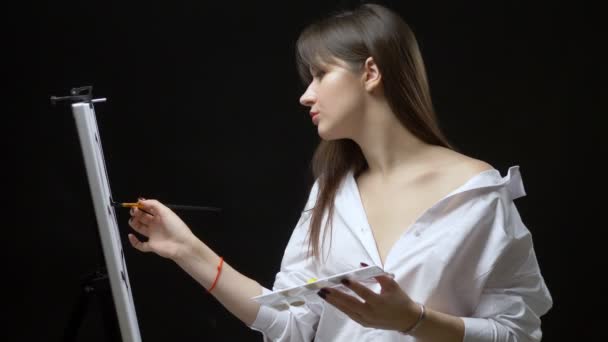 Güzel kız ressam tuvale yağlı boyalarla resim yapıyor. siyah arkaplan — Stok video