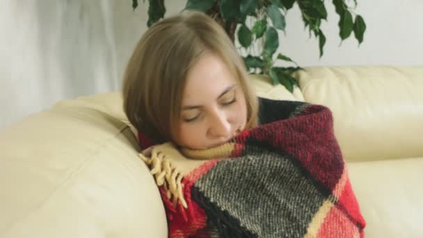 Retrato de una linda rubia. la chica sentada en el sofá, envuelta en una manta — Vídeo de stock