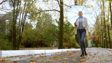 Parkta şemsiyeli kısa saçlı şık sarışın bir kadın.