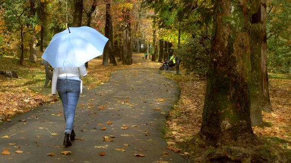 Femme en veste en cuir blanc marchant dans le parc d'automne avec un parapluie bleu — Photo