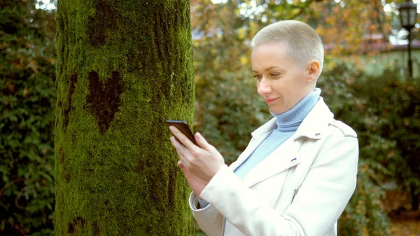 Женщина использует мобильный телефон, стоя рядом с деревом, на коре которого лает сердце — стоковое фото