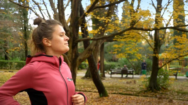 Belle femme avec des cheveux longs jogging dans le parc d'automne. vue latérale — Photo