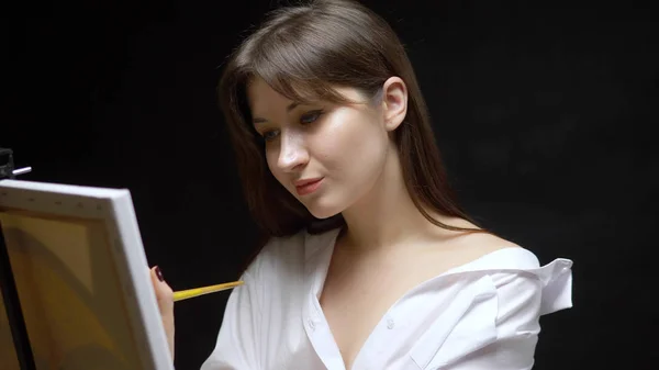 Cute girl artist paints a picture on canvas with oil paints. black background — Stock Photo, Image