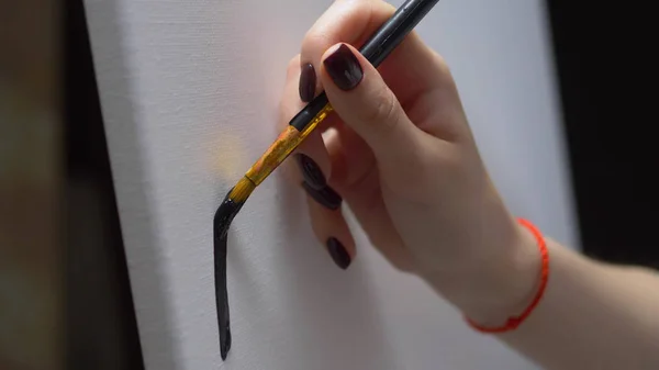 Fechar. pintura feminina à mão com uma escova uma linha preta em uma tela branca limpa — Fotografia de Stock
