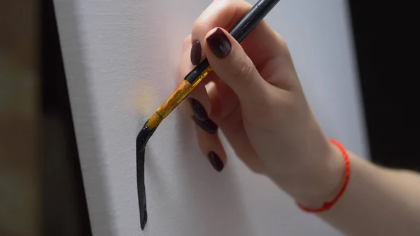 Een close-up. vrouwelijke hand schilderen met een borstel een zwarte lijn op een schone witte doek — Stockfoto