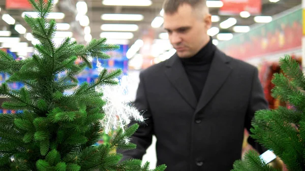 为圣诞节做准备。 男人在商店里挑一棵人造树 — 图库照片