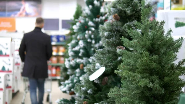 Förberedelser inför jul Nytt år. En man väljer ett konstgjort träd i butiken — Stockfoto