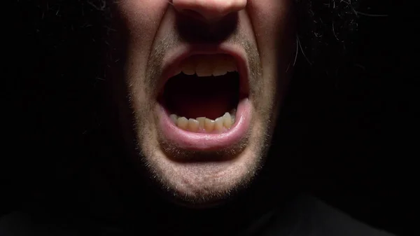 Detailní záběr. samčí ústa s křikem křivých zubů. Černé pozadí. — Stock fotografie