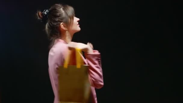 Chica elegante en traje rosa con bolsas de papel sobre fondo negro — Vídeo de stock