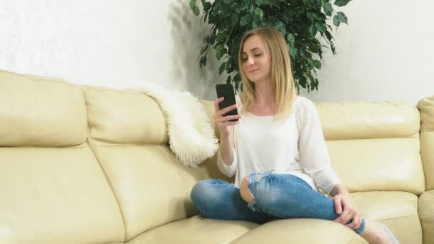 Διαταραγμένη κοπέλα χρησιμοποιεί ένα smartphone στο σπίτι κάθεται στον καναπέ. Άσχημα νέα. — Αρχείο Βίντεο