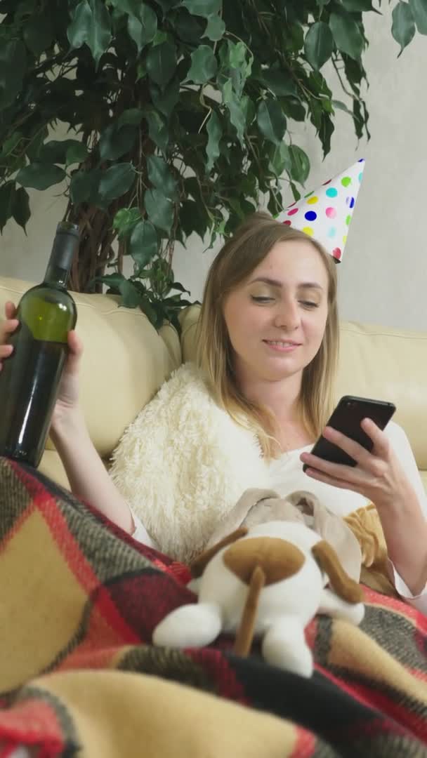 Dívka slaví svátky doma sama. pít a používat telefon. svisle — Stock video