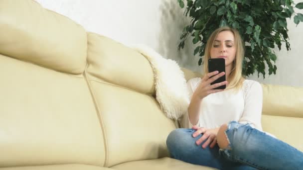 Rozrušená dívka používá doma smartphone, když sedí na gauči. špatná zpráva — Stock video