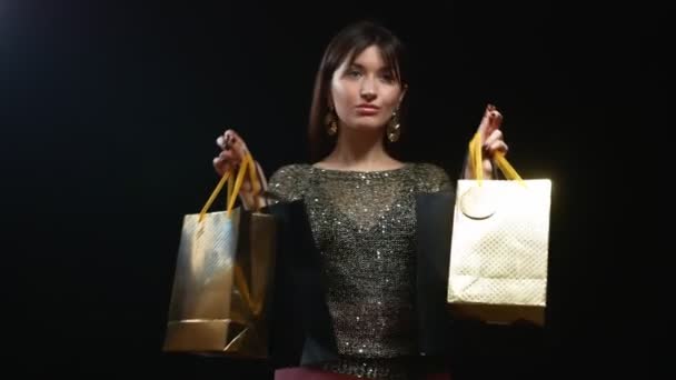 Schönes Mädchen in goldener Jacke mit Paketen auf schwarzem Hintergrund — Stockvideo