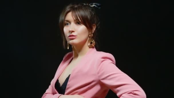 Flickan med de stora guld örhängen i rosa kostym danser på en svart bakgrund — Stockvideo