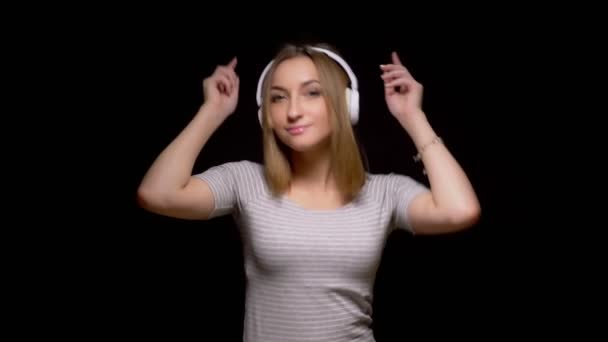 Cute young girl dancing in headphones on black background — Stock Video