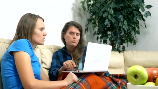 Duas meninas se sentam juntas no sofá na sala de estar e usando laptop — Vídeo de Stock