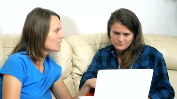 Duas meninas se sentam juntas no sofá na sala de estar e usando laptop — Vídeo de Stock