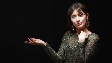 Siyah arka planda dans eden altın elbiseli ve büyük altın küpeli bir kız.