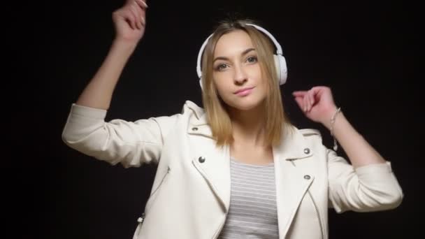 Cute girl in white headphones and a white leather jacket on black background — Stock Video