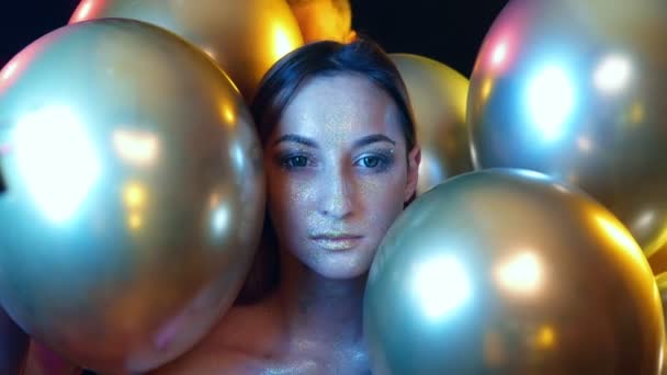 Nahaufnahme Mädchengesicht mit goldenen Pailletten unter den goldenen Luftballons — Stockvideo
