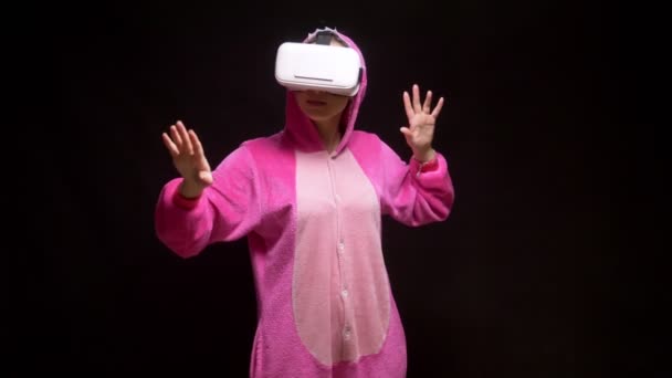 Menina de pijama rosa kigurumi em óculos VR em um fundo preto. festa de pijama — Vídeo de Stock