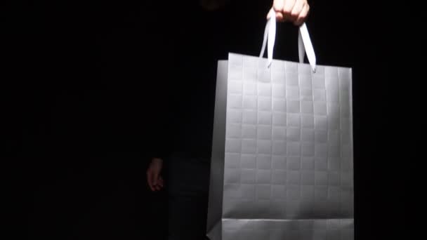 Рука держит пакет на черном фоне. скопировать пространство. покупка, продажа, скидка — стоковое видео