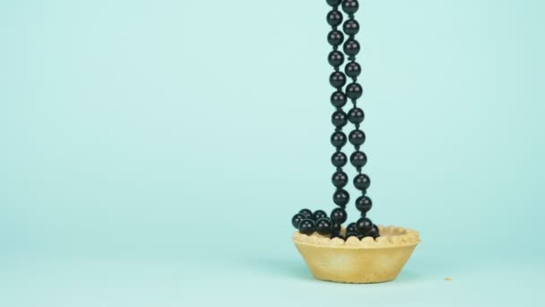 Mode konst. minimalism. De svarta pärlorna faller ner i tartlet. blå bakgrund — Stockvideo