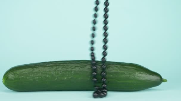 Trendige Kunst Food Design. Gurke mit einer Kette schwarzer Perlen. blauer Hintergrund — Stockvideo