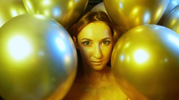 Лицо девушки крупным планом с золотыми блестками среди золотых воздушных шаров — стоковое видео