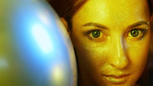 Close-up meisje gezicht met gouden pailletten tussen de gouden ballonnen — Stockvideo