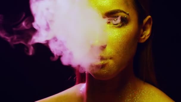 Крупним планом дівчина обличчям з золотими блискітками. дим з рота — стокове відео