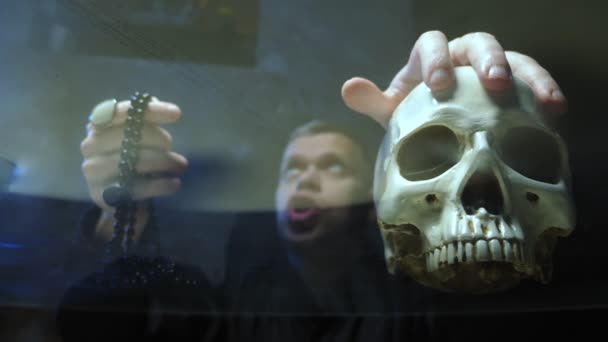 ガラスのカウンター越しに見ることができます魔術師は呪文を唱える頭蓋骨に手をかけて — ストック動画