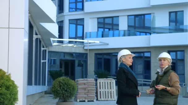 Twee vrouwen in witte helmen praten op de achtergrond van het gebouw — Stockvideo