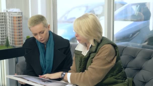 Dos mujeres están hablando, sentado en la oficina de ventas en el fondo de la disposición del edificio — Vídeos de Stock