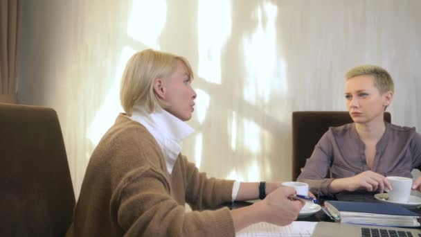 Δύο γυναίκες μιλάνε ενώ κάθονται σε ένα γραφείο μπροστά από ένα λάπτοπ. — Αρχείο Βίντεο