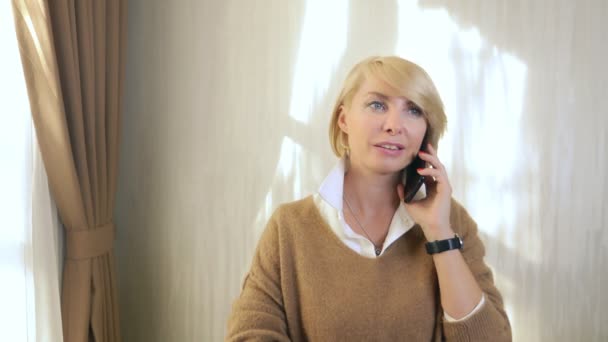Bela mulher falando em um telefone celular, de pé no escritório pela janela — Vídeo de Stock