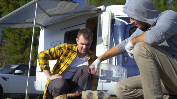 Zwei Männer kochen Fleisch auf dem Grill in der Nähe der Wohnmobile in der Natur — Stockvideo