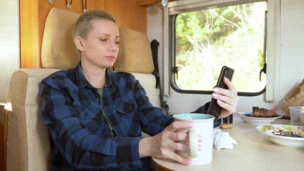 Vrouw gebruikt een mobiele telefoon terwijl zitten aan een tafel in een camper — Stockvideo