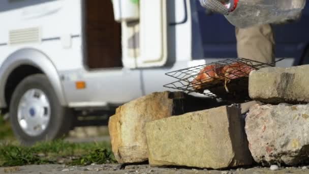 Um homem cozinha carne na grelha ao ar livre em um fundo de autocaravanas — Vídeo de Stock